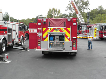 This stainless steel pumper shows a functional rear step hydraulic rescue tool compartment and a swing-down ladder rack