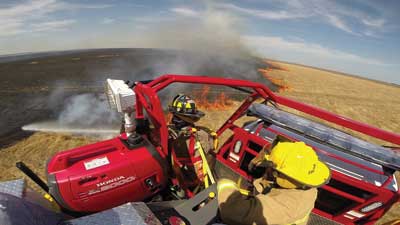 1 One tactic for fighting fine-fuels fires involves a firefighter riding on the apparatus exterior aiming a water stream directly at the base of the fire. Apparatus used for this tactic typically include a platform behind the cab where a firefighter can stand. (Photo courtesy of Blanchat Mfg. Inc