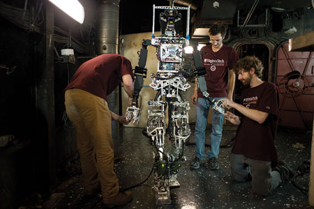 5 Virginia Tech researchers John Seminatore, left, and Jack Newton, kneeling, adjust SAFFIR’s arms before the firefighting test on board the USS Shadwell, while James Burton observes. 