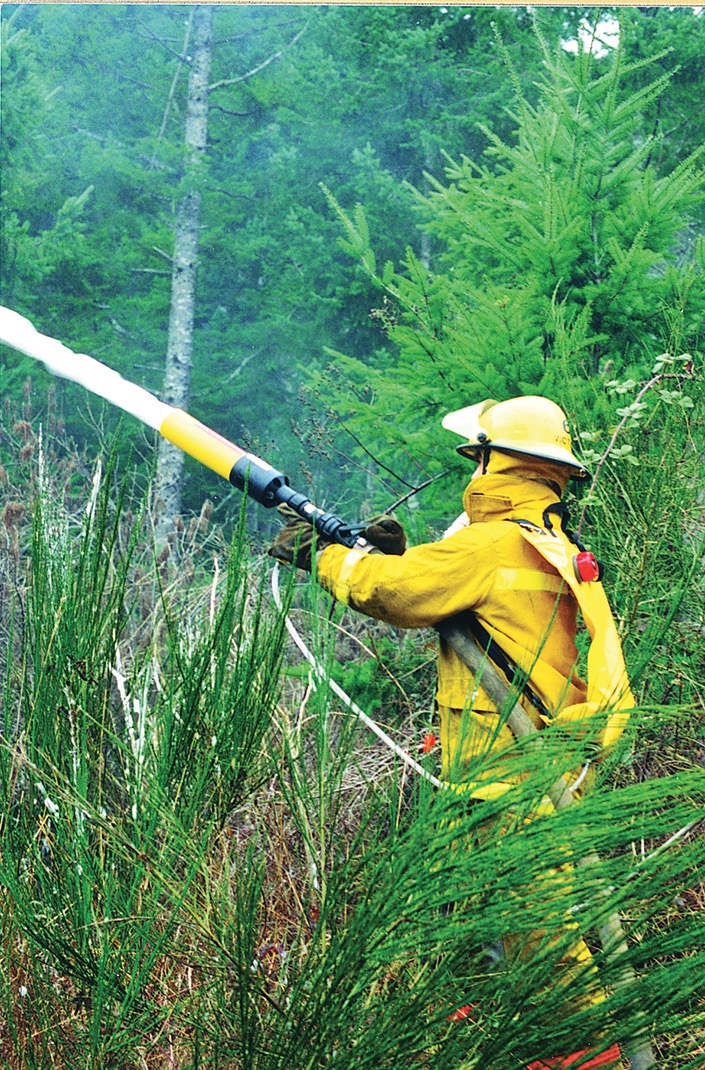 A wildland firefighter uses a Scotty Firefighter foam eductor backpack system to fight a wildland fire