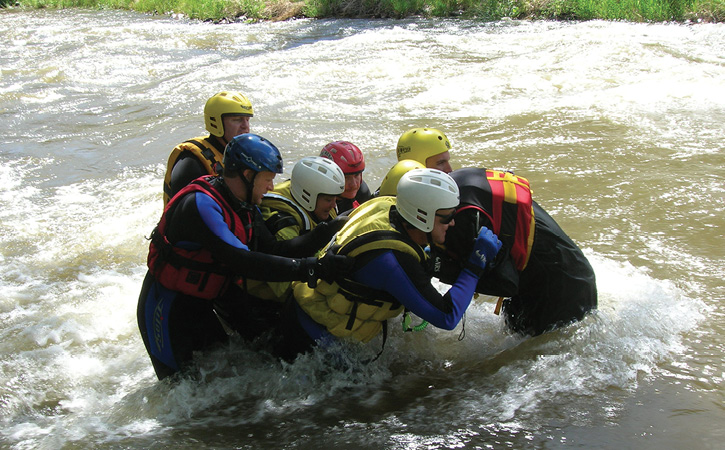 A wade crew of rescuers snatches a victim from swift water and walks him to safety on shore.