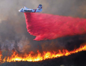 A CAL FIRE C-130-H aircraft makes a drop of 4,000 gallons of retardant on a wildland fire. (Photo courtesy of CAL FIRE.)