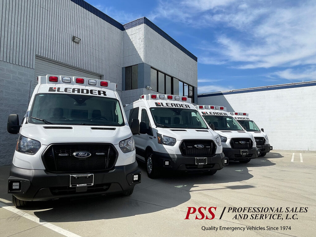 Four white ambulances are backed up next to a building.